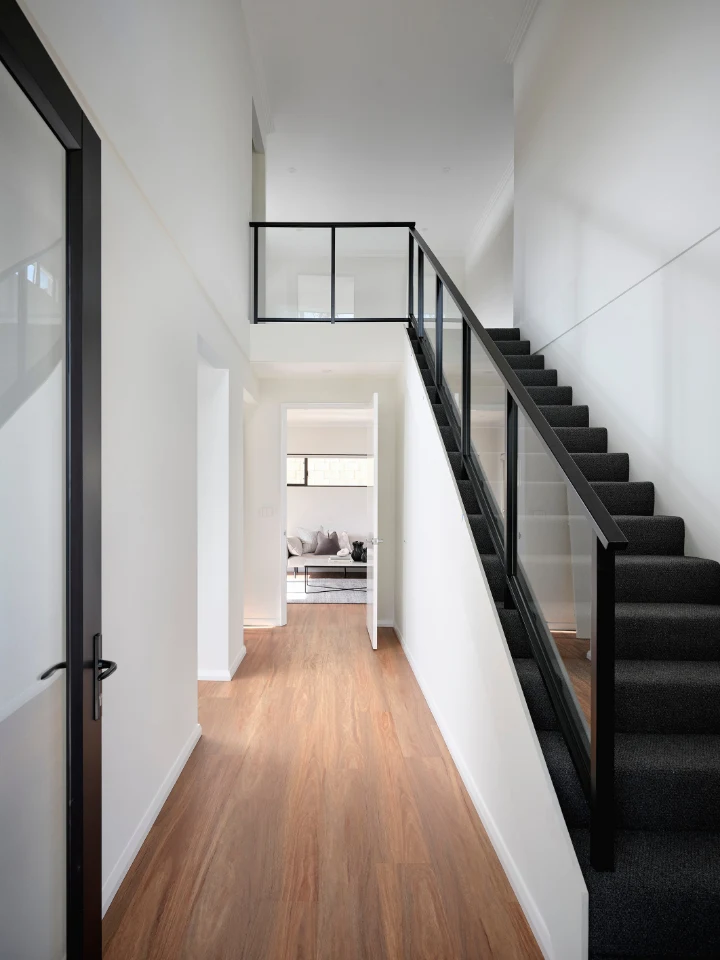 Modern hallway with wooden flooring and sleek black staircase leading to airy loft space.