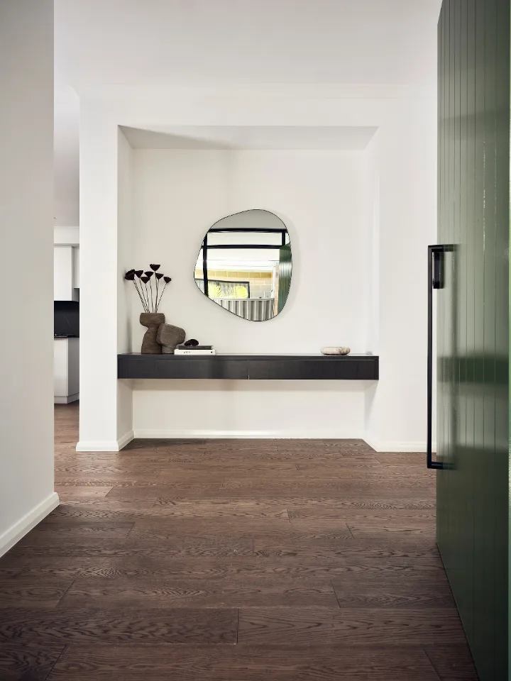 Minimalist hallway interior with unique mirror, floating shelf, and wooden flooring.
