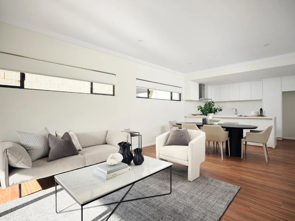 Modern minimalist living room with gray sofa, armchair, and open kitchen design.