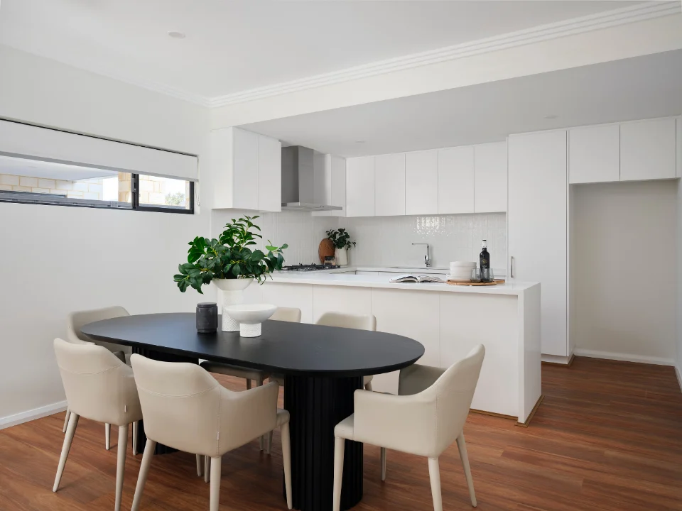 Modern kitchen with white cabinets, wood flooring, and a black dining table surrounded by beige chairs.