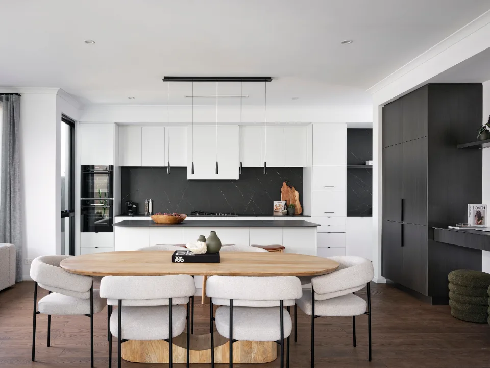 Modern kitchen with white cabinets, black backsplash, wooden dining table, and beige chairs.