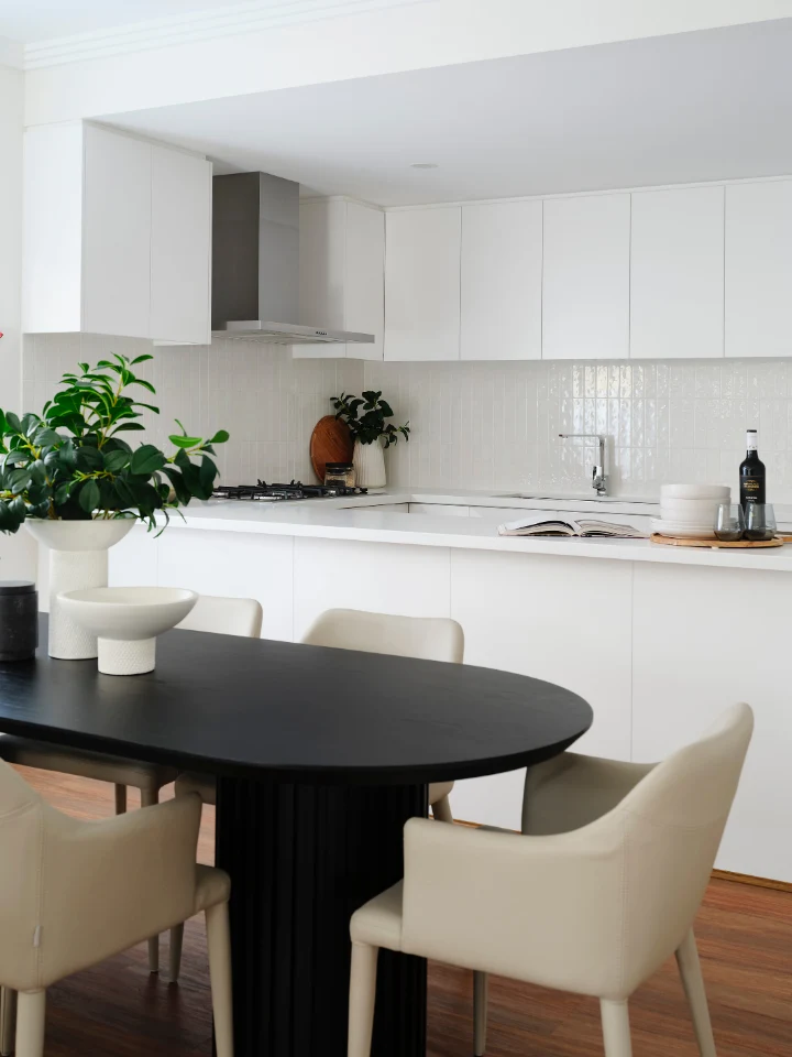 Modern minimalist kitchen with white cabinets, black dining table, and potted plant for a fresh, clean look.