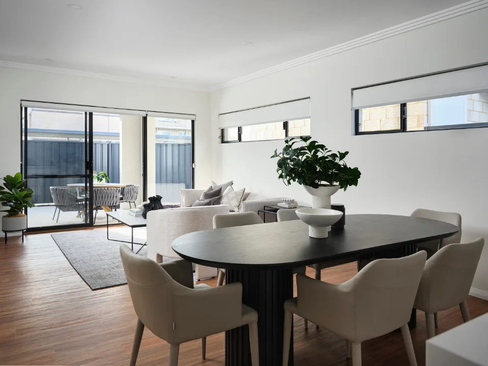 Modern open-plan living room with dining area, white walls, large windows, and elegant furniture.