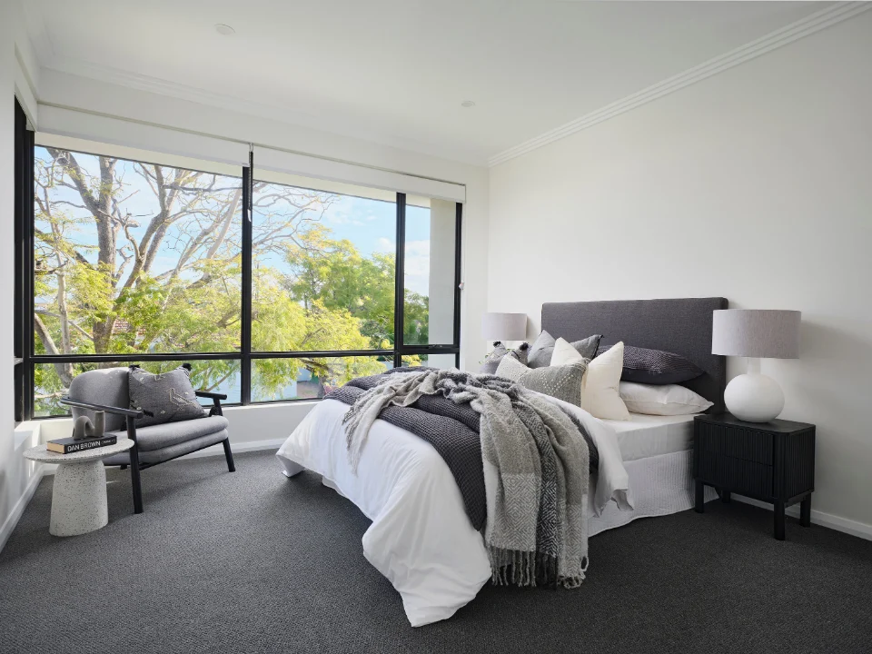 Modern bedroom with large windows, stylish gray and white decor, and cozy textiles for a relaxing atmosphere.