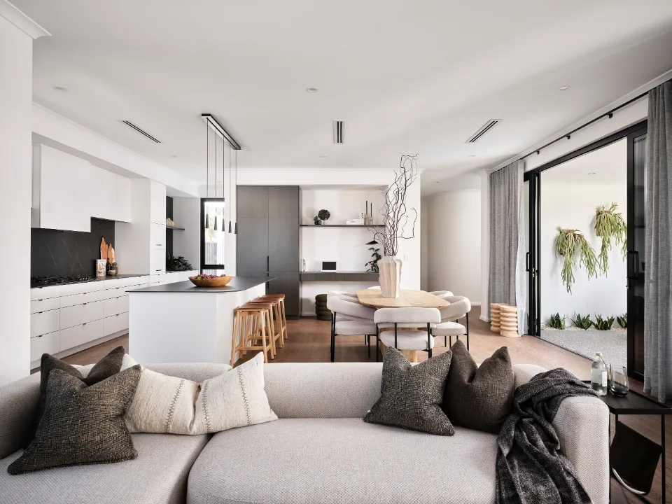 Modern open-plan living room and kitchen with neutral decor and large windows.