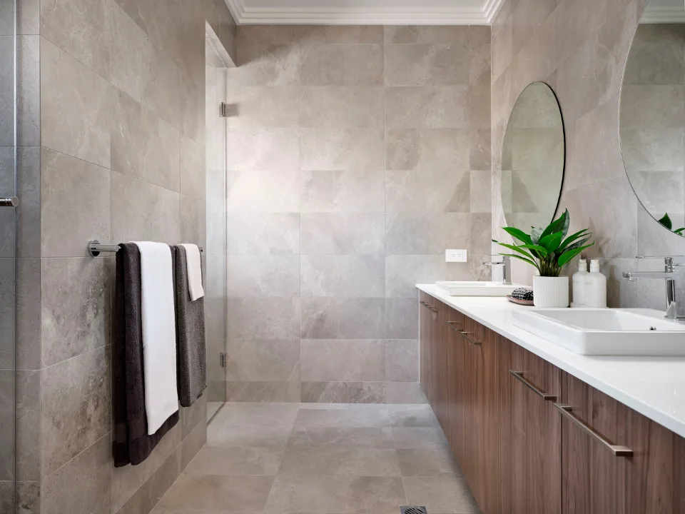 Modern bathroom with gray tiles, wooden vanity, round mirror, and green plant.
