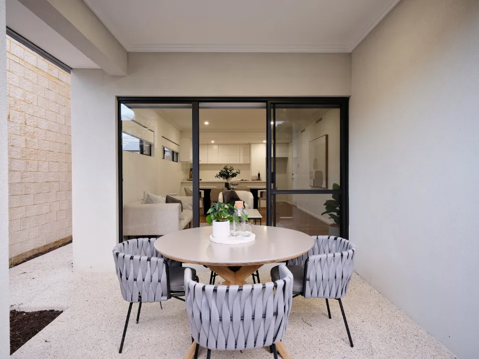 Modern outdoor patio with round table and four chairs, view into stylish interior living room.