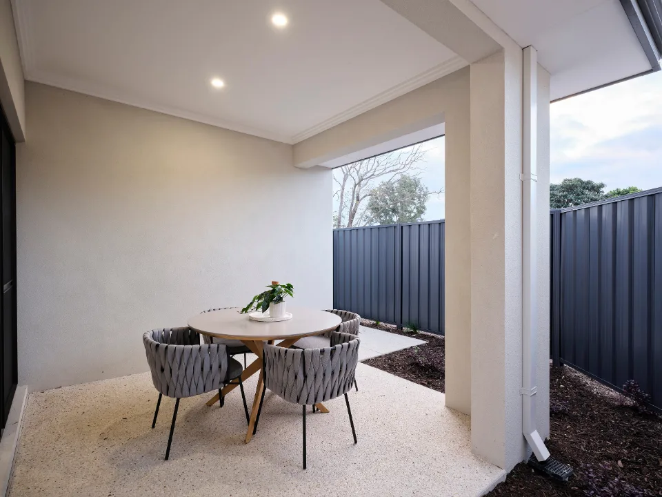 Covered outdoor patio with round table and chairs, surrounded by privacy fencing and garden space.