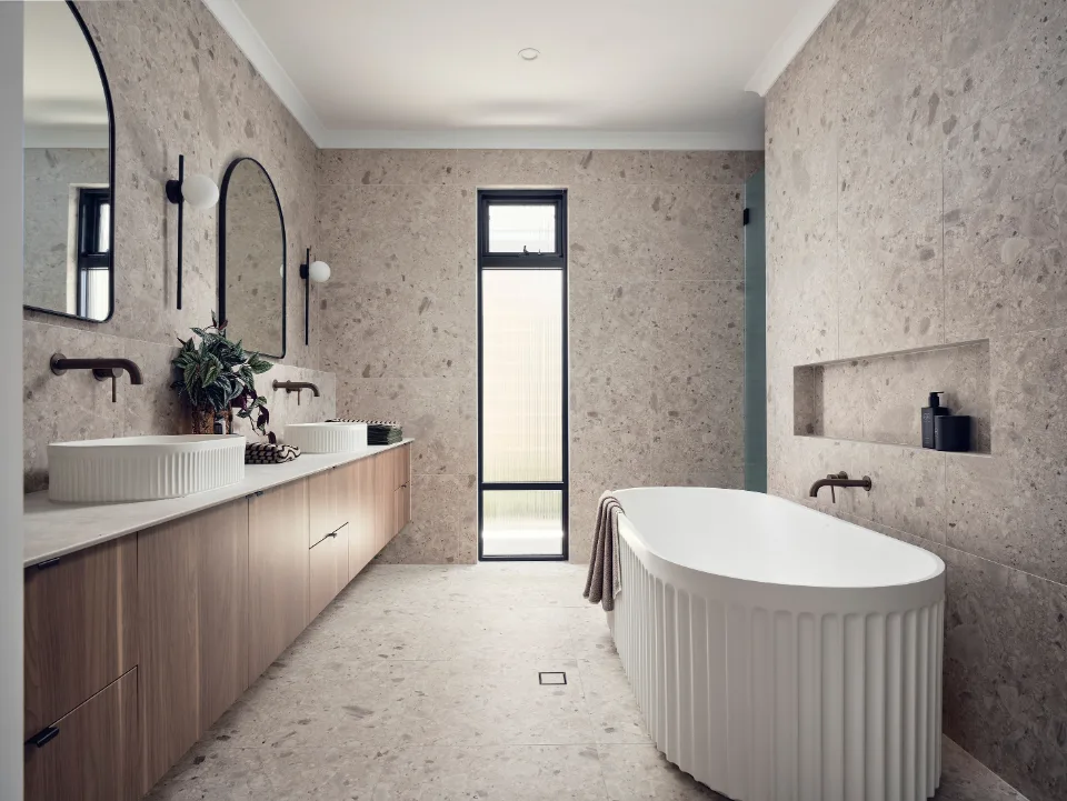 Modern bathroom with freestanding tub, double sinks, and elegant lighting fixtures against stone walls.