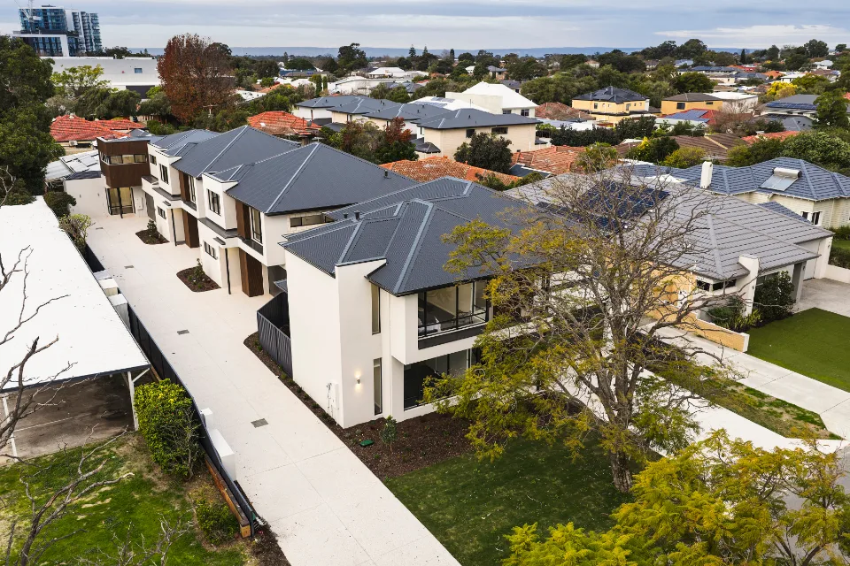 Modern suburban homes with grey roofs, aerial view showing residential neighborhood and trees.