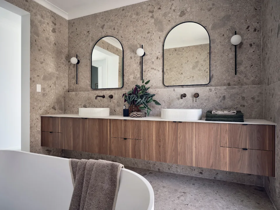 Modern bathroom with dual sinks, wooden vanity, and large mirrors on a stone wall.
