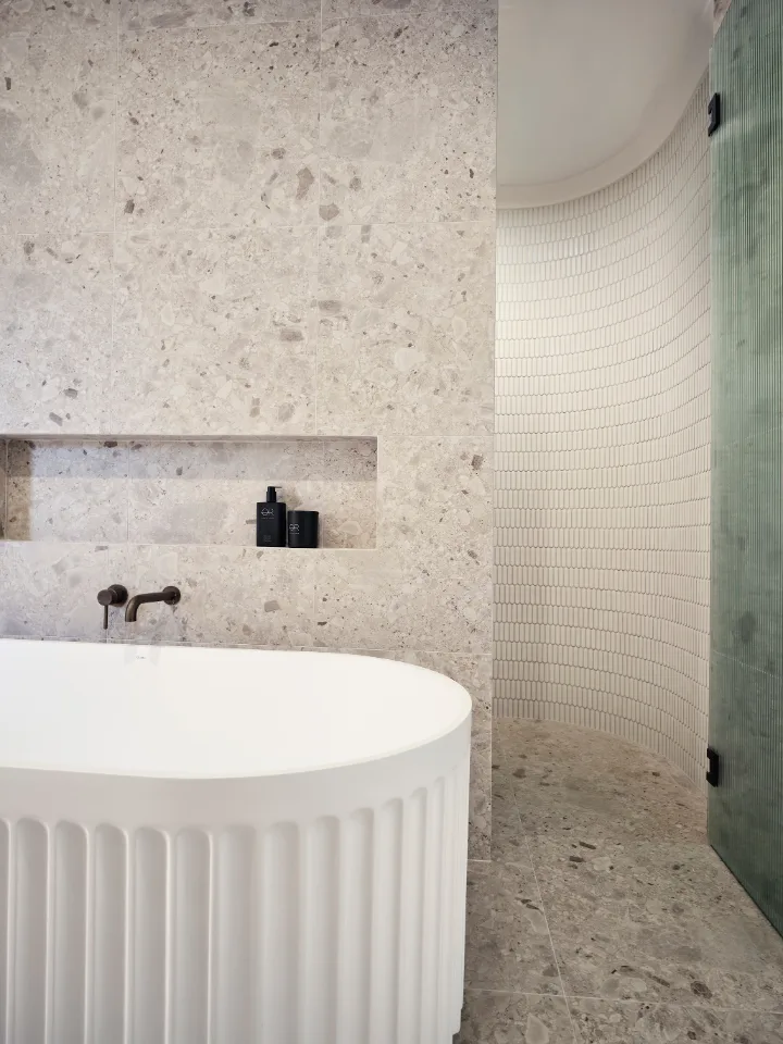 Modern bathroom with a freestanding white bathtub and textured stone walls.