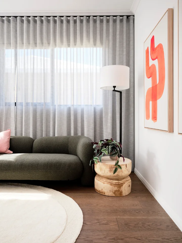 Modern living room with a gray sofa, wooden side table, floor lamp, and abstract wall art.