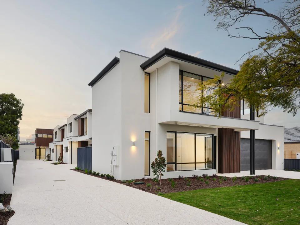 Modern two-story house with large windows and a paved driveway at dusk.