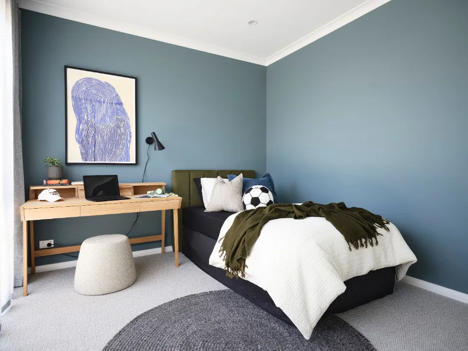 Cozy modern bedroom with desk, laptop, and artwork on blue wall.