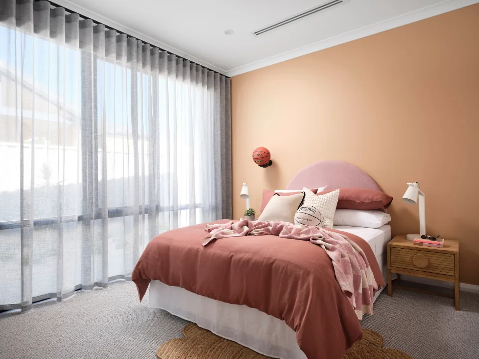 Modern bedroom with peach accents, large window, and stylish decor.