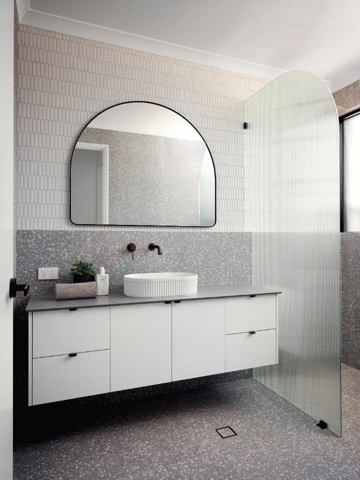 Modern bathroom with floating vanity, round mirror, and glass shower screen.