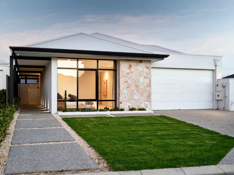 Modern single-story home with large windows, stone facade, and landscaped front yard at sunset.