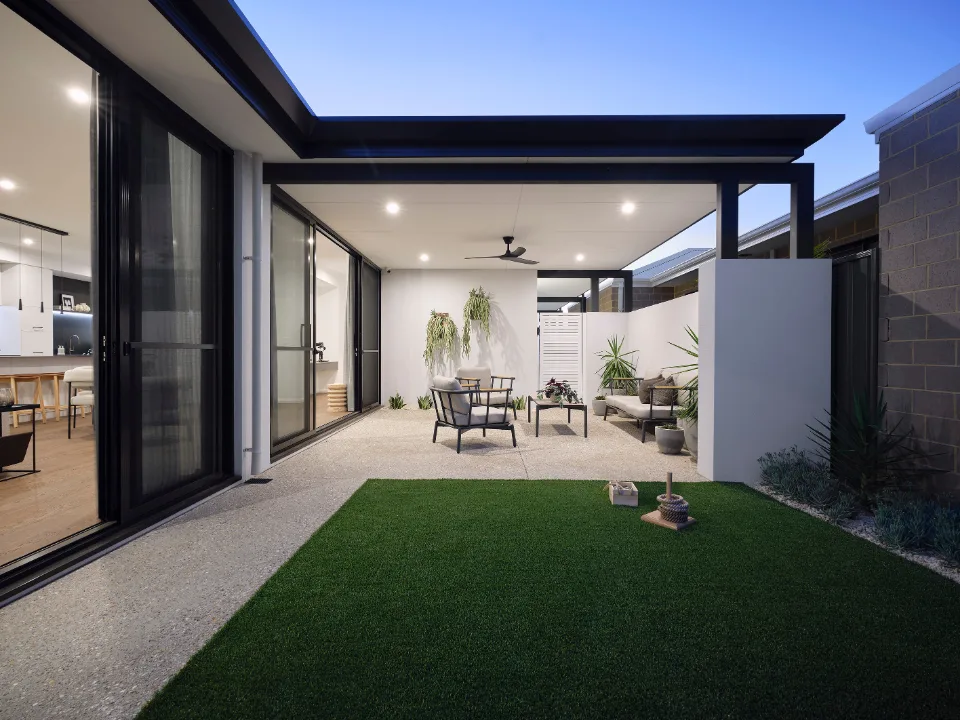 Modern patio with seating, green lawn, and evening lighting in a stylish outdoor space.
