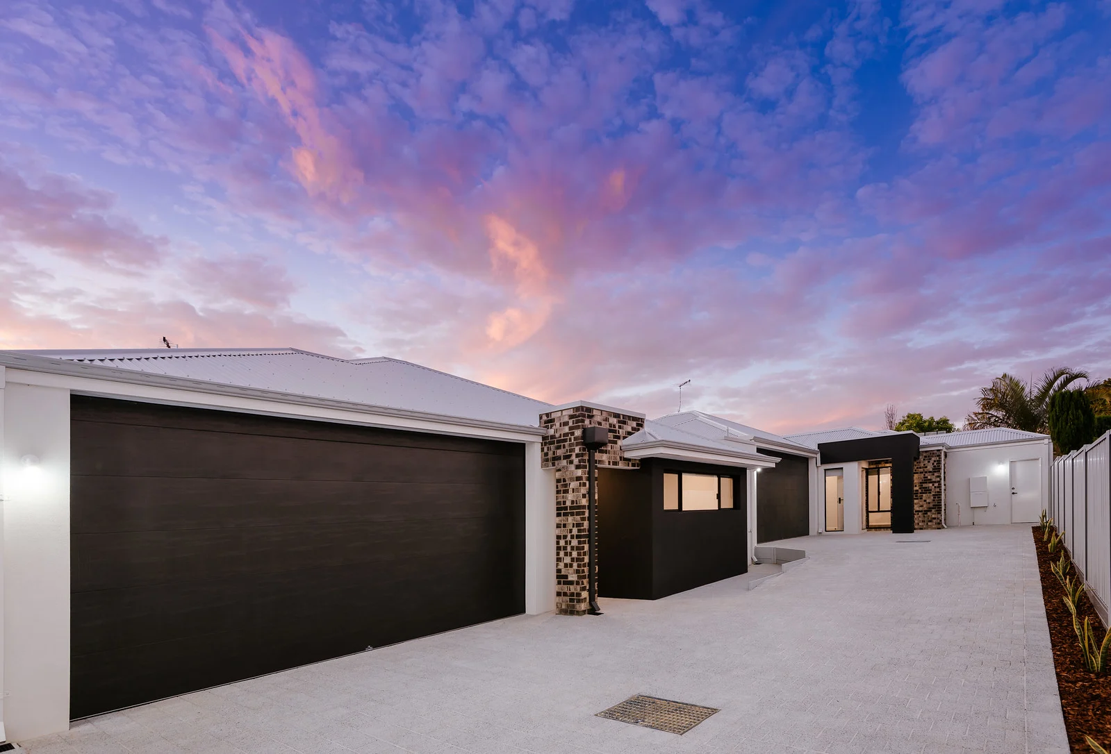 Modern house exterior with sunset sky, featuring a large driveway and black garage door.