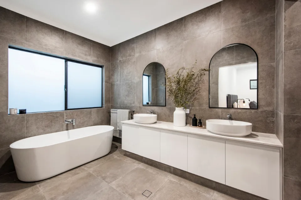 Modern bathroom with freestanding bathtub, dual sinks, and large mirrors on tiled walls.