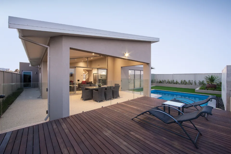 Modern backyard patio with lounge chairs, pool, and dining area at sunset.