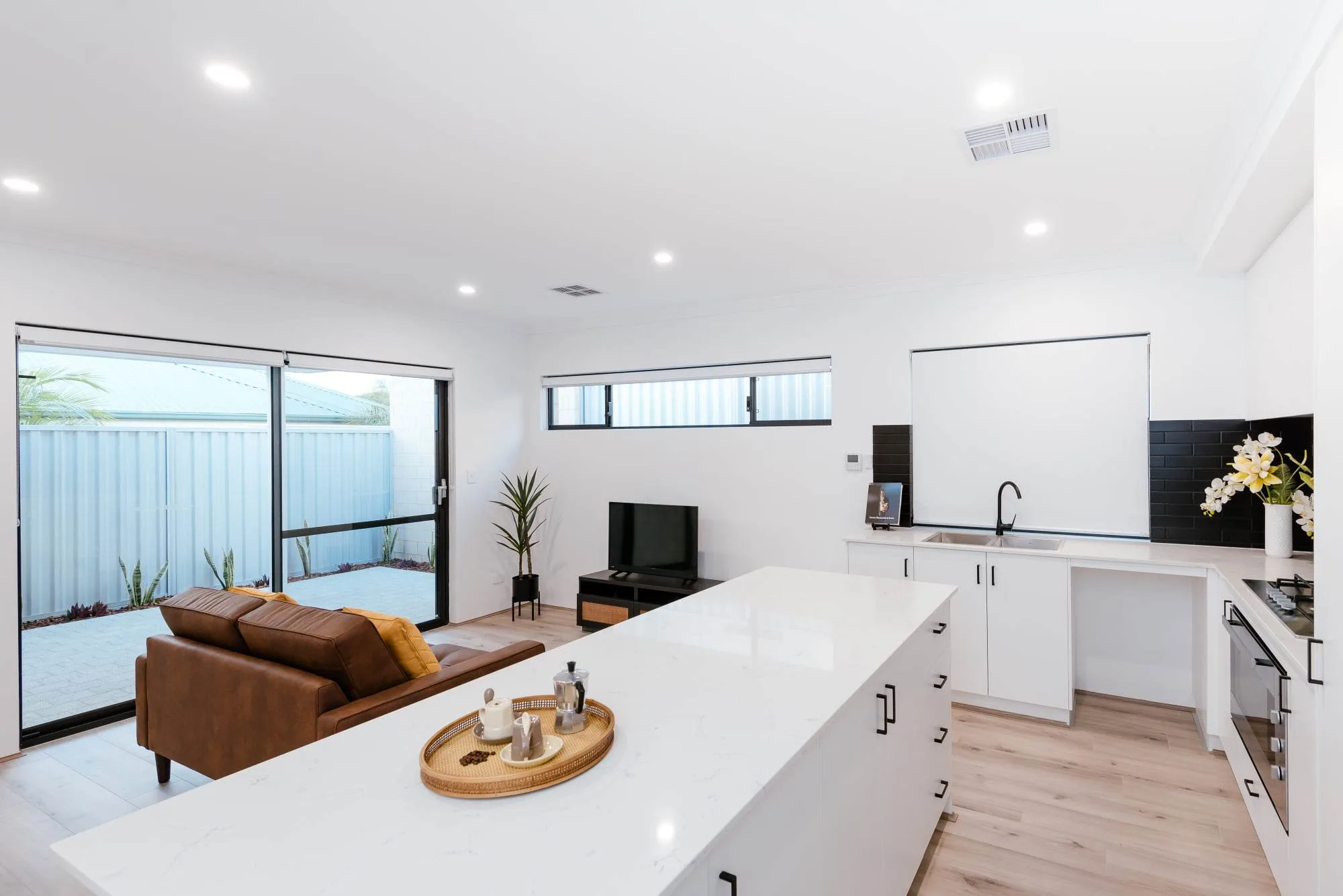 Modern open-plan kitchen and living area with white countertops and brown sofa.
