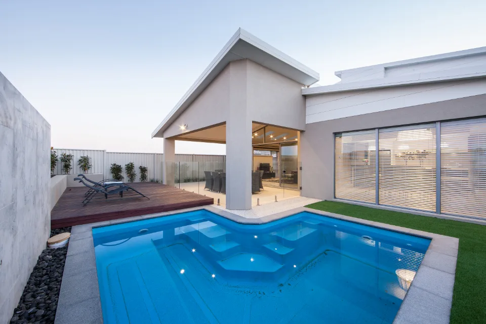 Modern backyard patio with pool and lounge chairs at sunset.