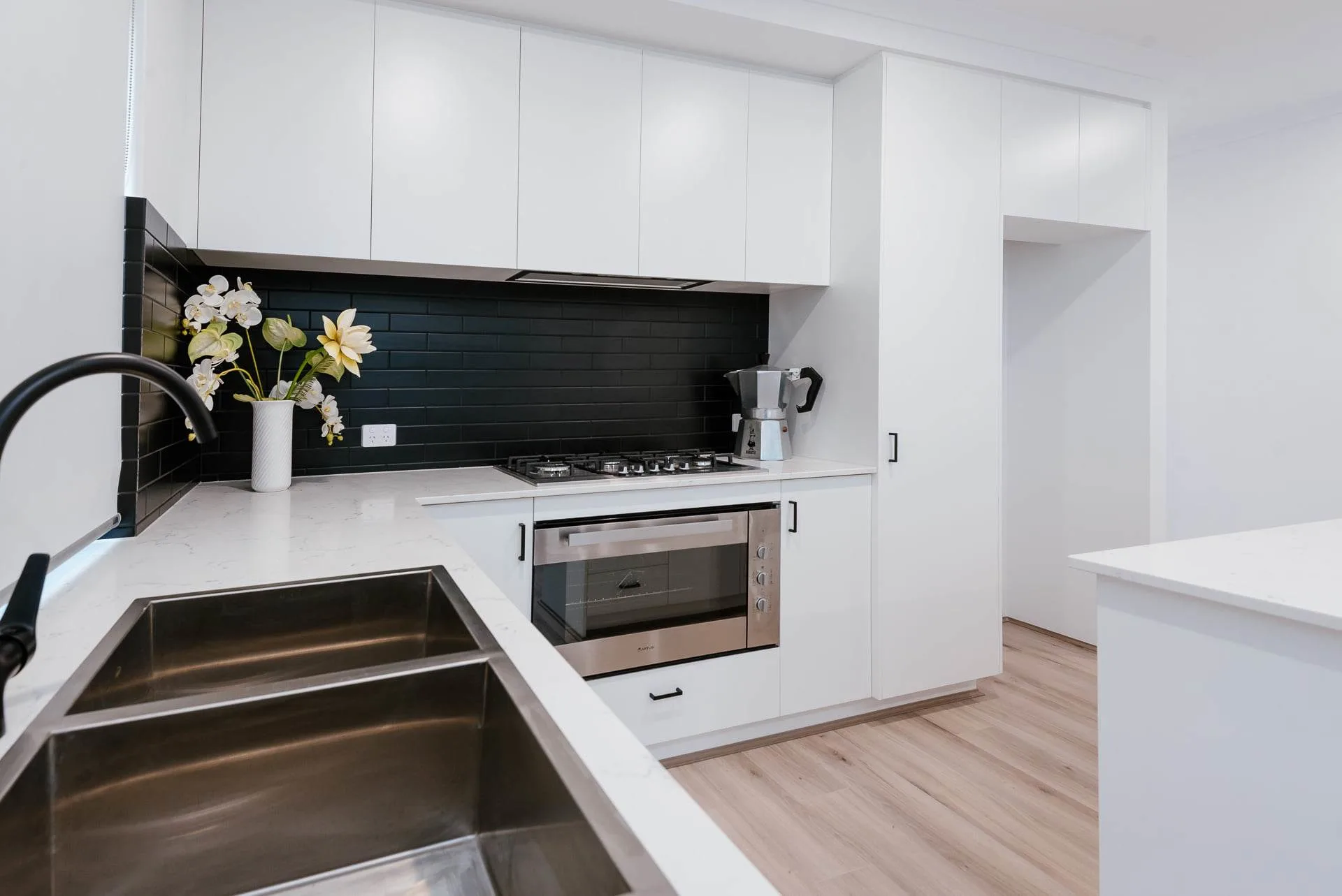 Modern kitchen interior with white cabinets, black backsplash, stainless steel appliances, and a flower vase on the counter.