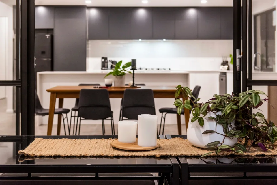 Modern kitchen with dining table, plants, and candles, featuring sleek black cabinetry and ambient lighting.
