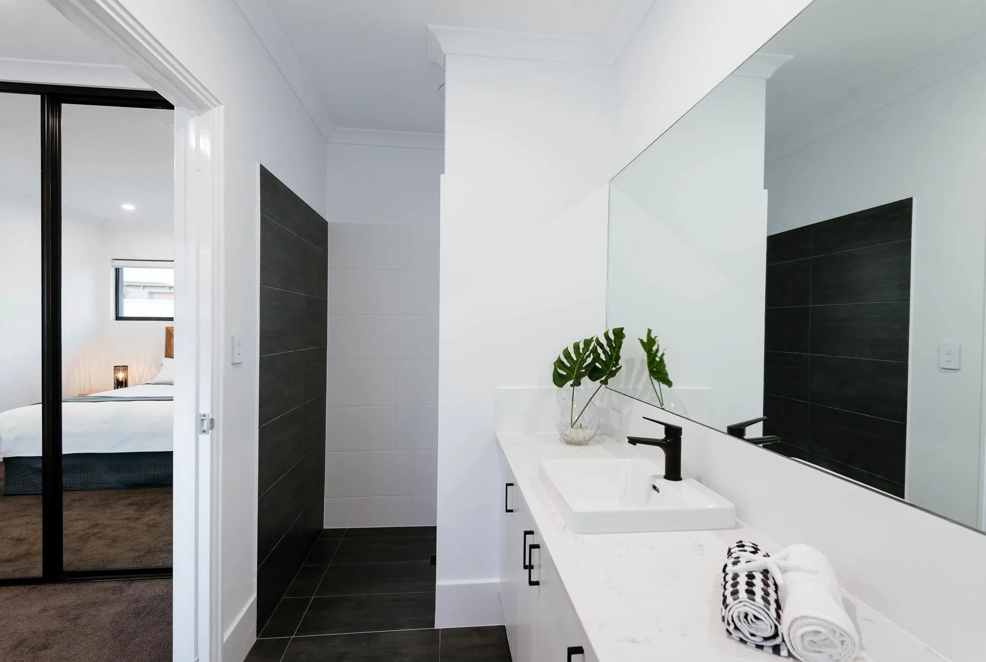 Modern bathroom with white vanity, black faucet, large mirror, and plant decor in a minimalist style.