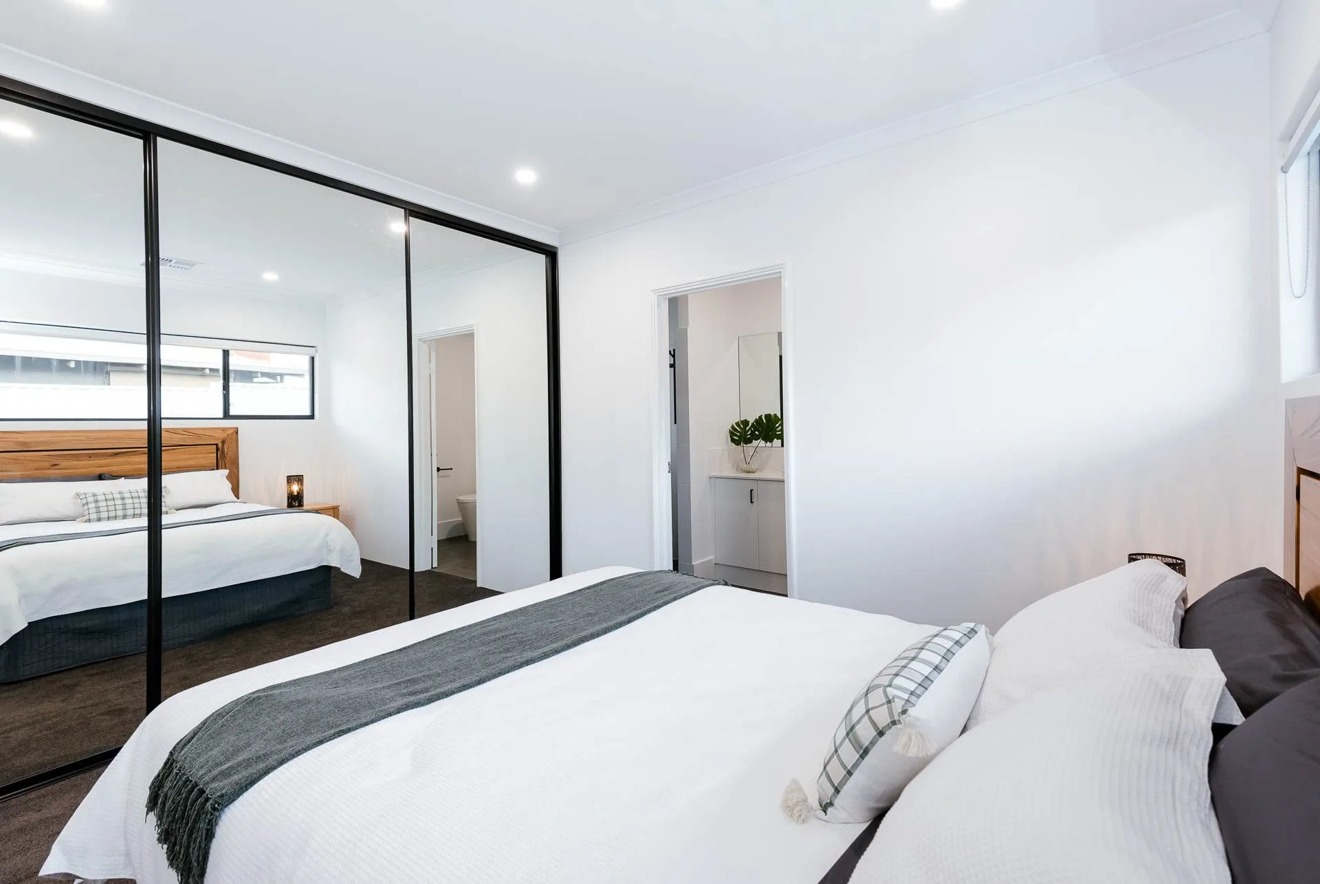 Modern bedroom with white bedding, mirrored wardrobe, and ensuite bathroom for a stylish and cozy living space.