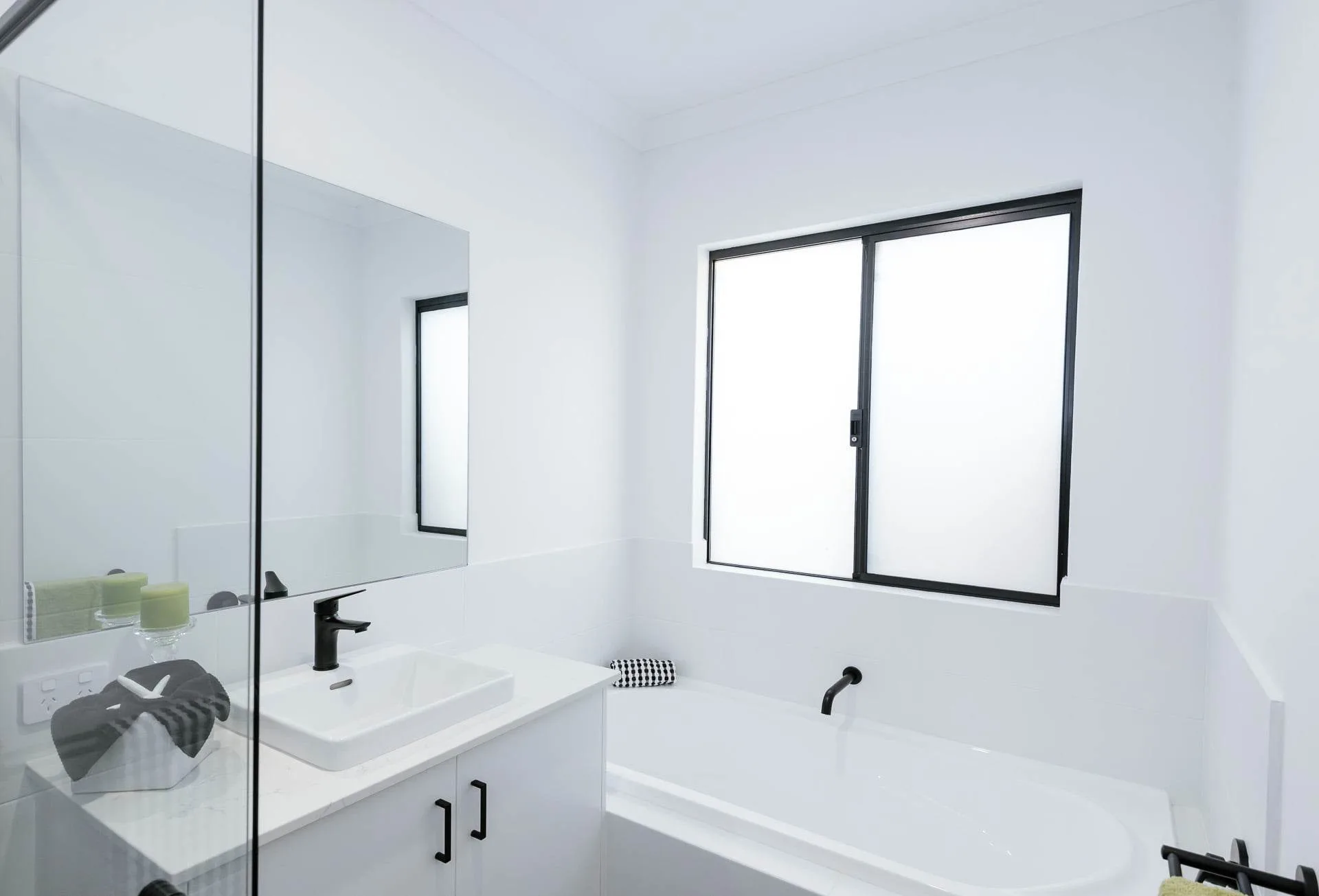 Modern minimalist bathroom with white sink, black faucet, and large window.