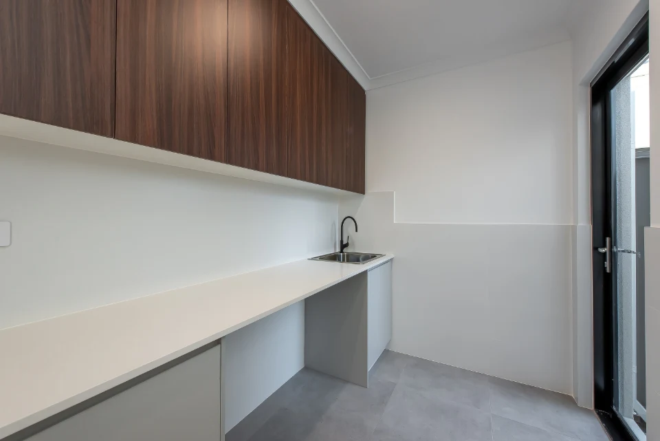 Modern utility room with white countertop, wood cabinets, and sink near the door for space-efficient design.