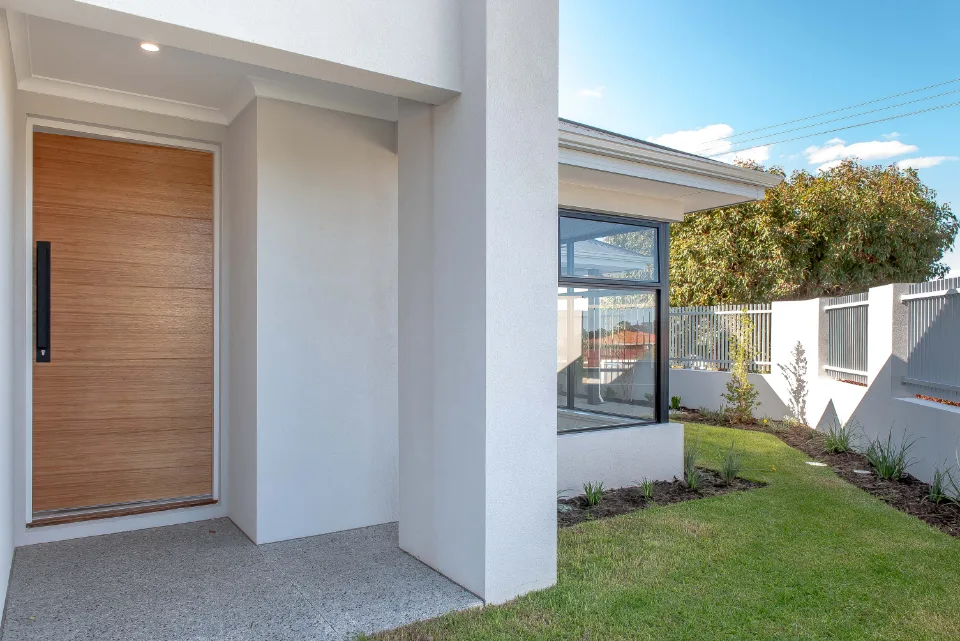 Modern house entrance with wooden door and landscaped garden path.