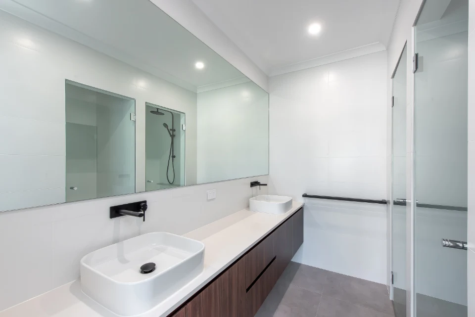 Modern bathroom with large mirror, double sinks, glass shower, and sleek design.