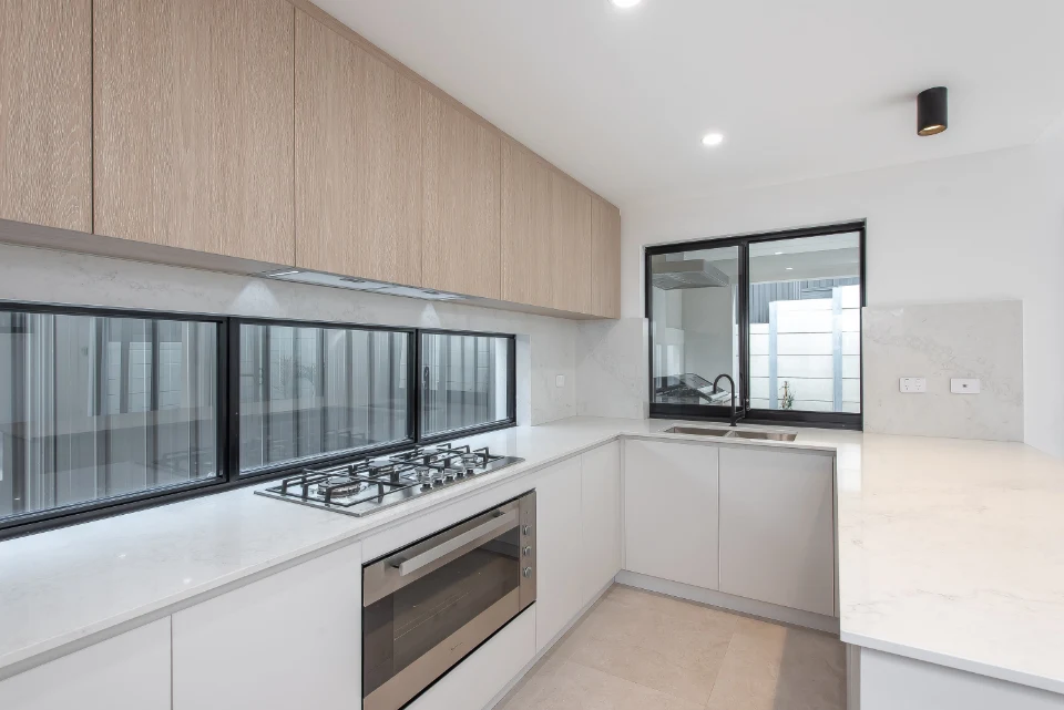 Modern kitchen with white countertops, gas stove, light wood cabinets, and large windows for natural light.