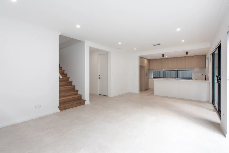 Modern open-plan kitchen and living area with hardwood staircase and neutral tones.