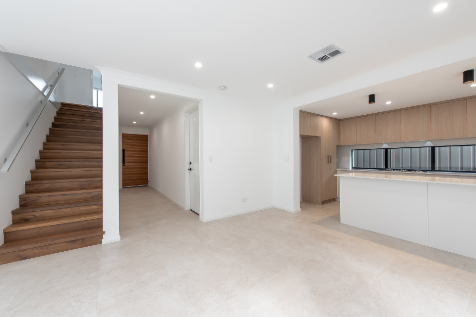 Modern open-concept kitchen and living space with wooden staircase and ample natural light.