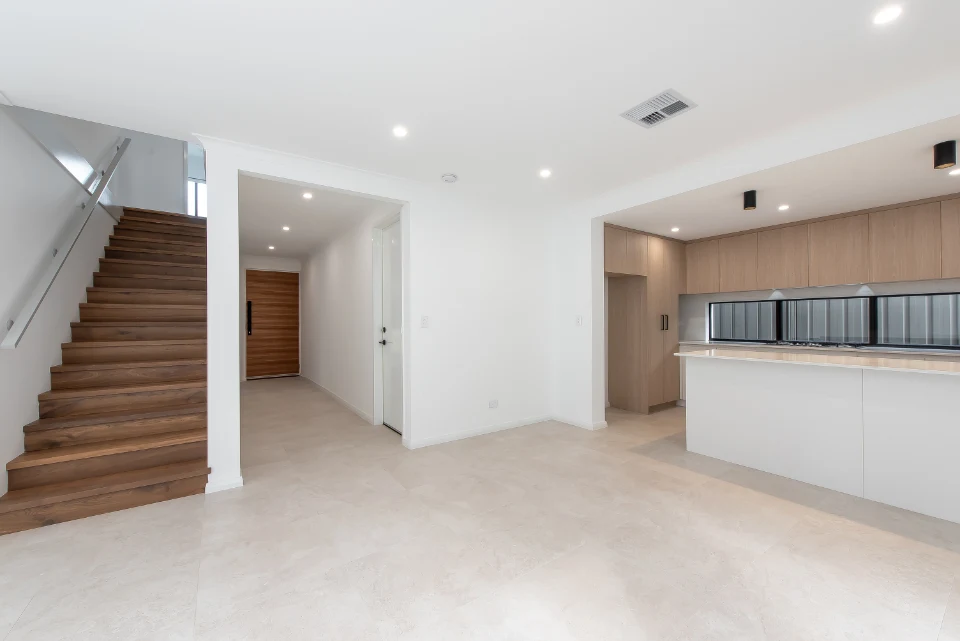 Modern open-concept kitchen and living area with wooden staircase, bright lighting, and stylish cabinetry.