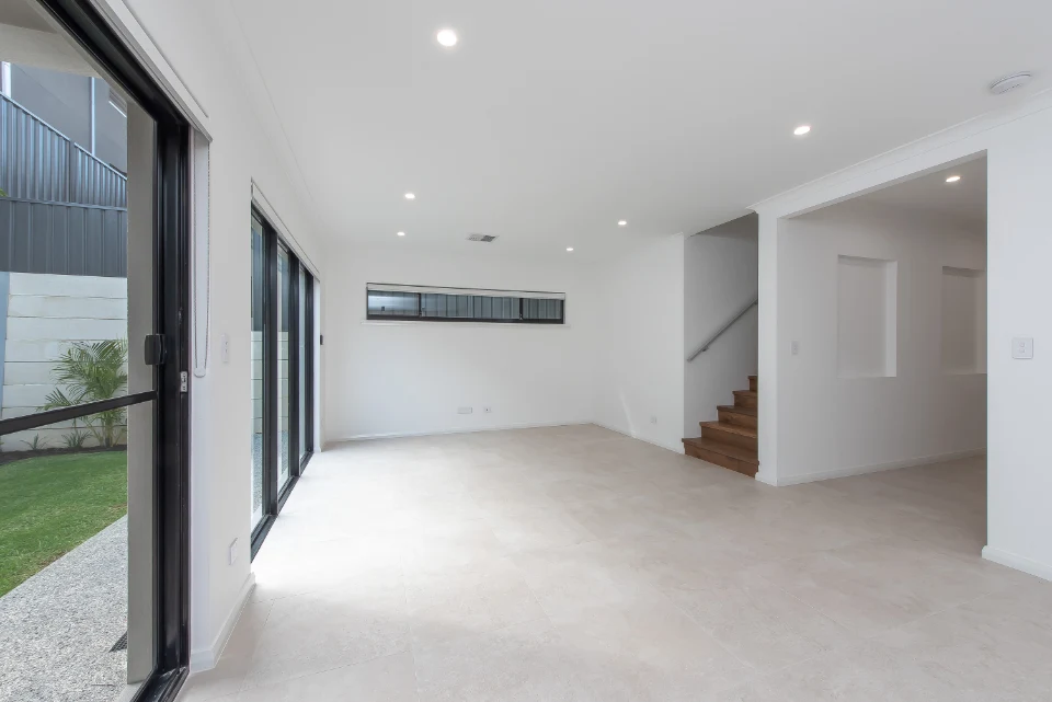 Modern living room with white walls, large windows, and tile flooring leading to a staircase and garden view.