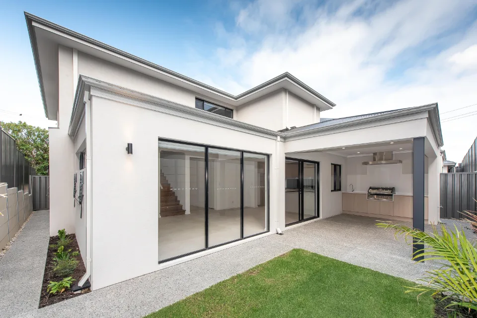 Modern two-story house with large windows and outdoor kitchen area.