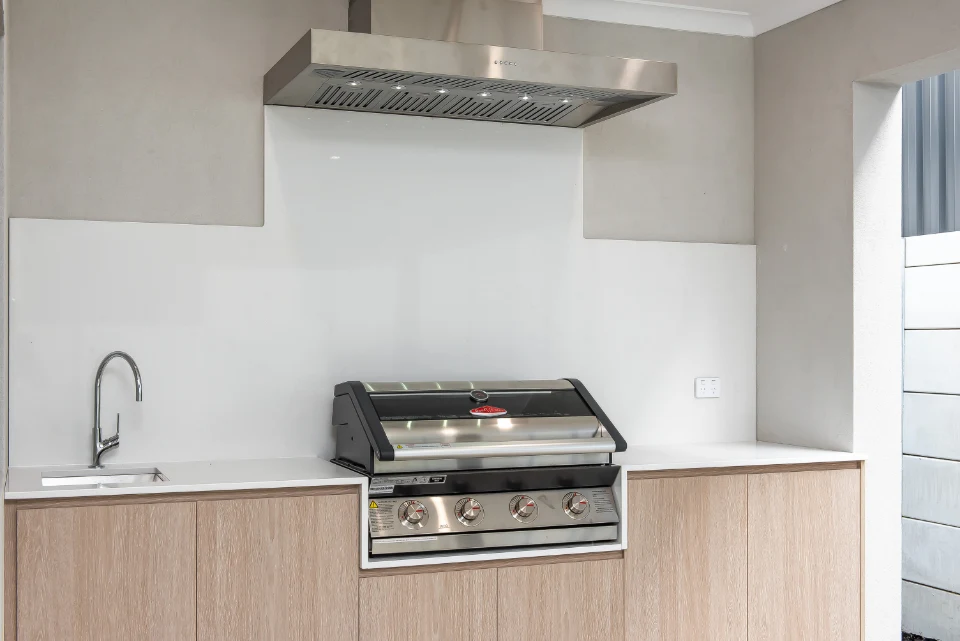 Outdoor kitchen with stainless steel grill, wooden cabinets, and sink. Ideal for modern patio cooking setups.
