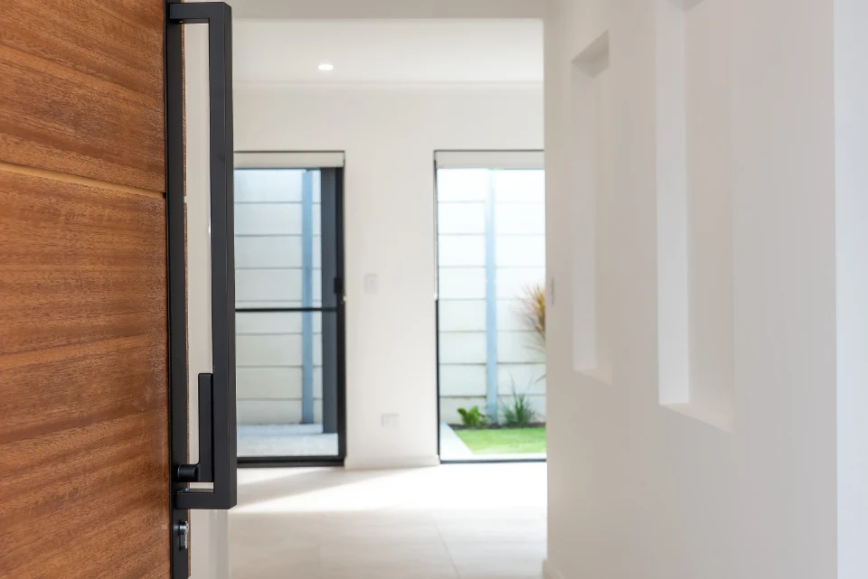 Modern wooden door opening to a bright interior hallway with garden view.