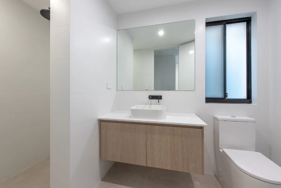 Modern minimalist bathroom with wooden vanity, large mirror, and natural light.