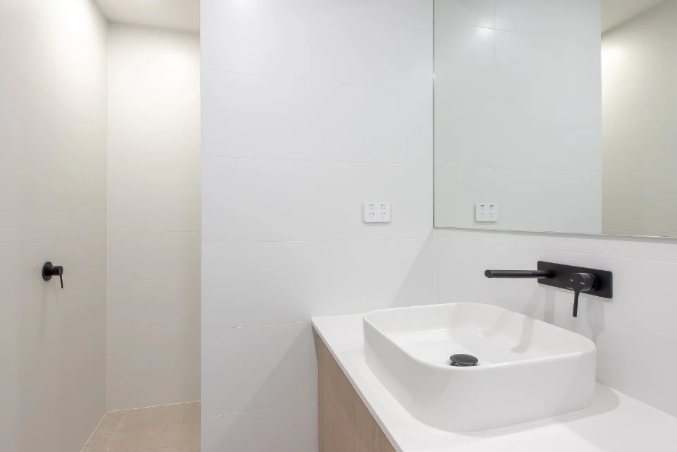Modern minimalist bathroom with white sink and sleek black fixtures.