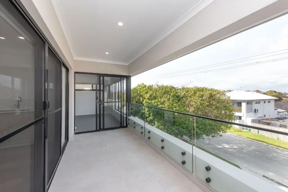 Modern balcony with glass railing overlooking neighborhood greenery.