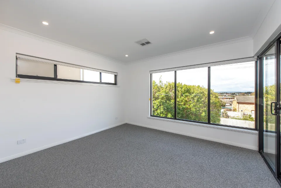 Empty modern room with large windows offering a scenic view, carpet flooring, and white walls.