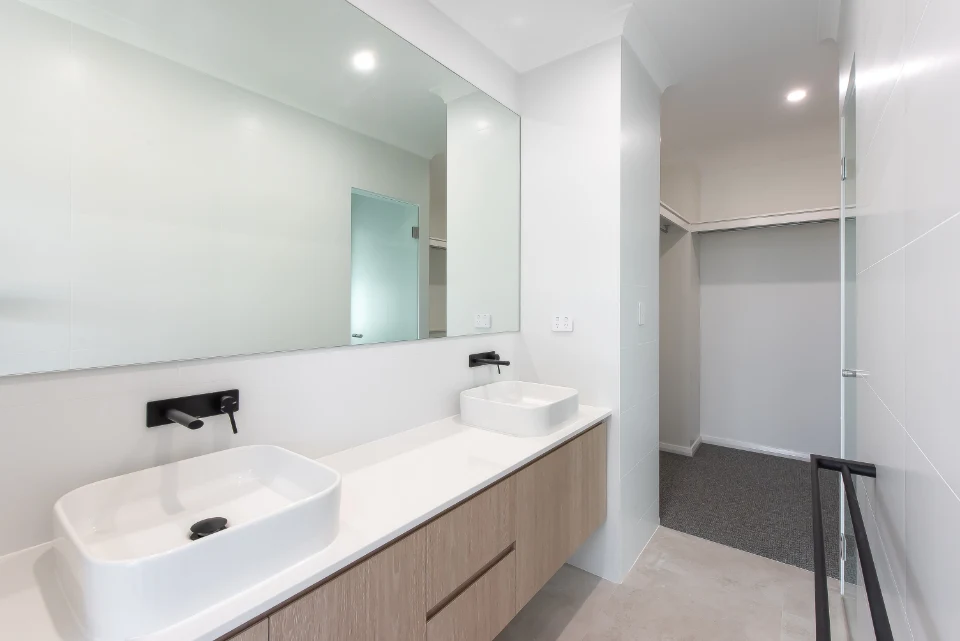 Modern bathroom with double sinks and wood vanity, featuring a large mirror and open closet in minimalist design.