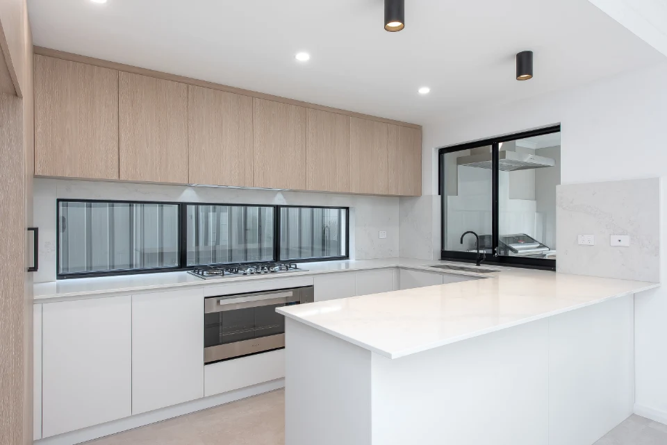 Modern kitchen with white countertops, light wood cabinets, and stainless steel stove.